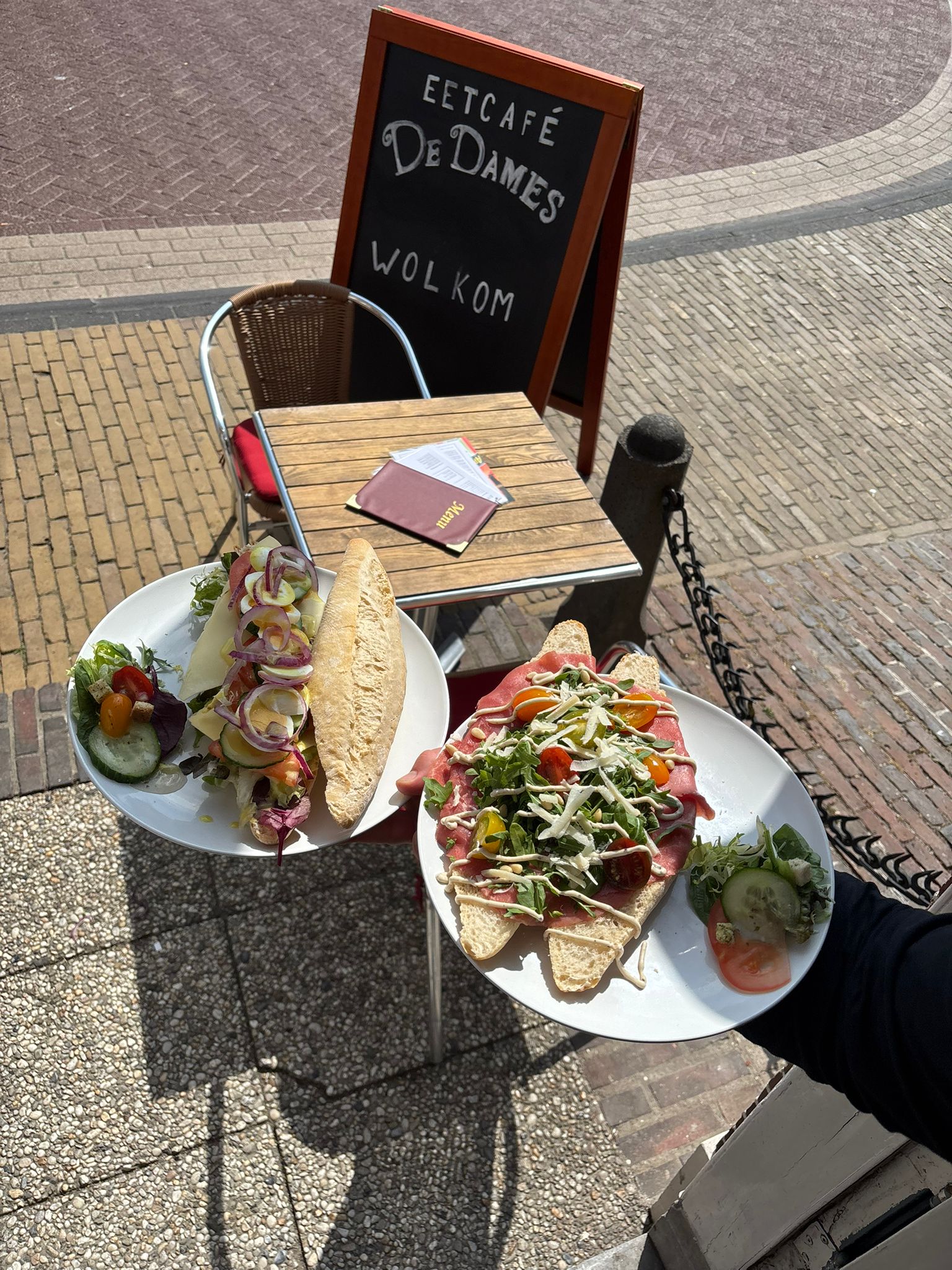 Terras van restaurant Eetcafé De Dames in Balk, Friesland, met welkomstbord en verse gerechten op tafel